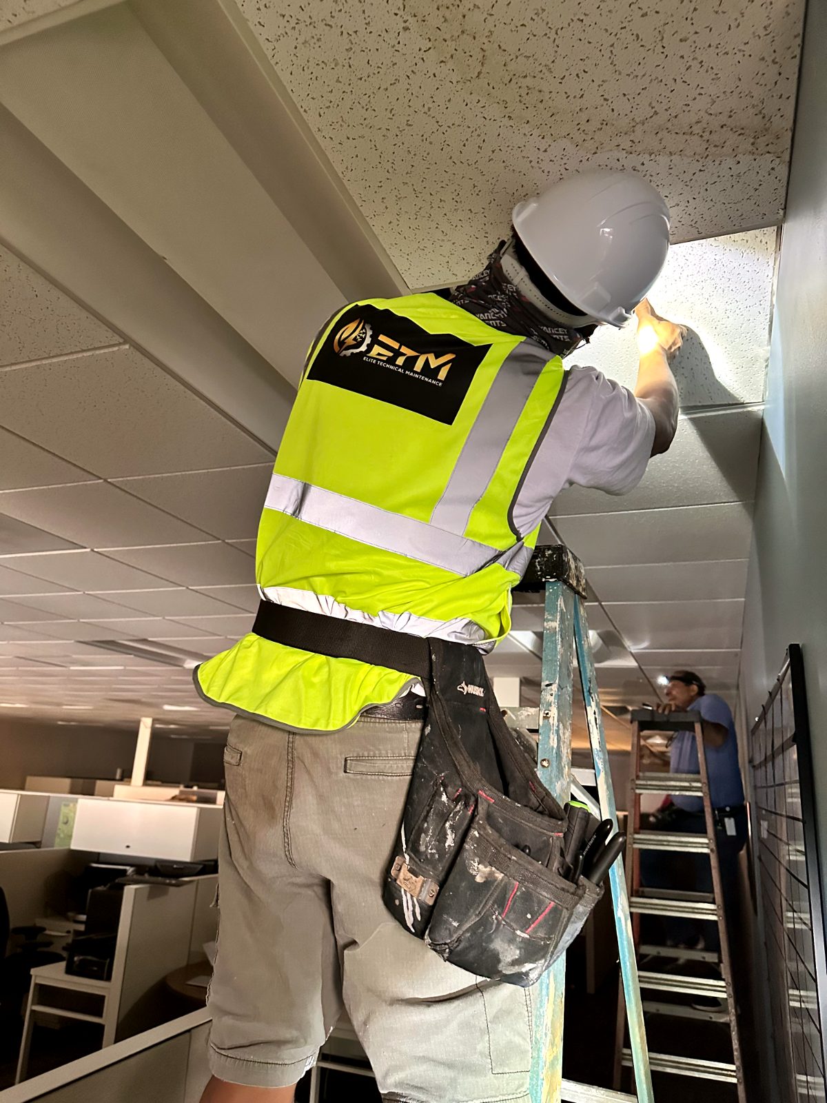 ETM technician working from a ladder on ceiling maintenance